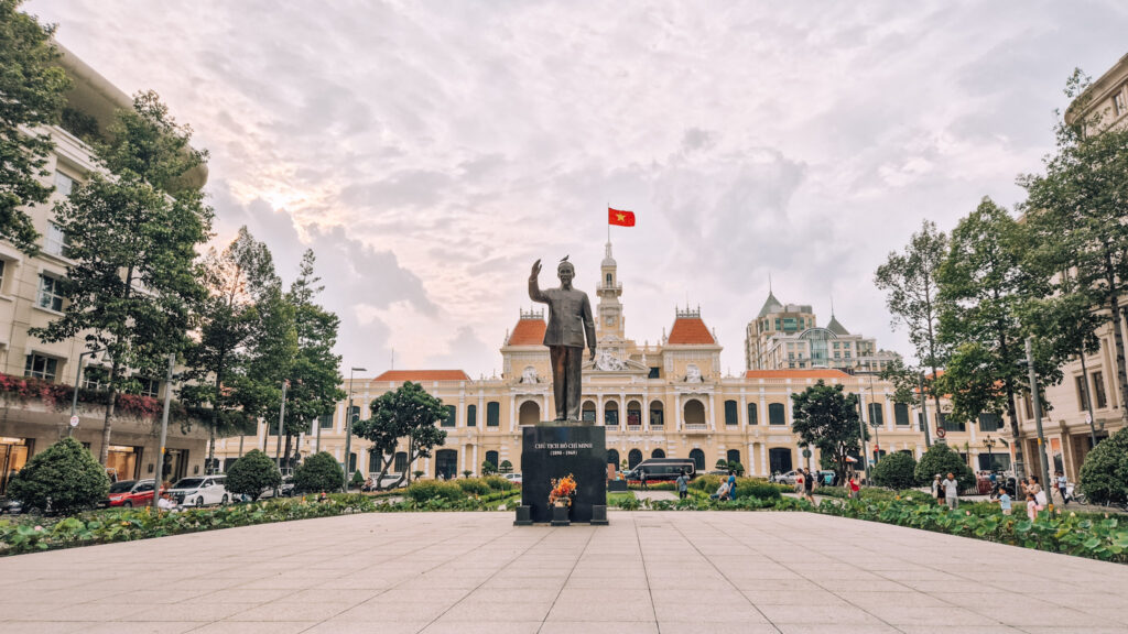 Statue of Ho Chi Minh City in front of a colonial building with a large Vietnamese flag.