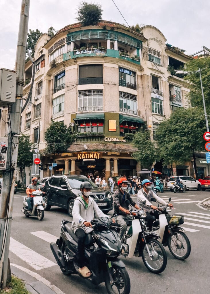 Motorbikes and cars on a street in front of the Catinat Building in Saigon.