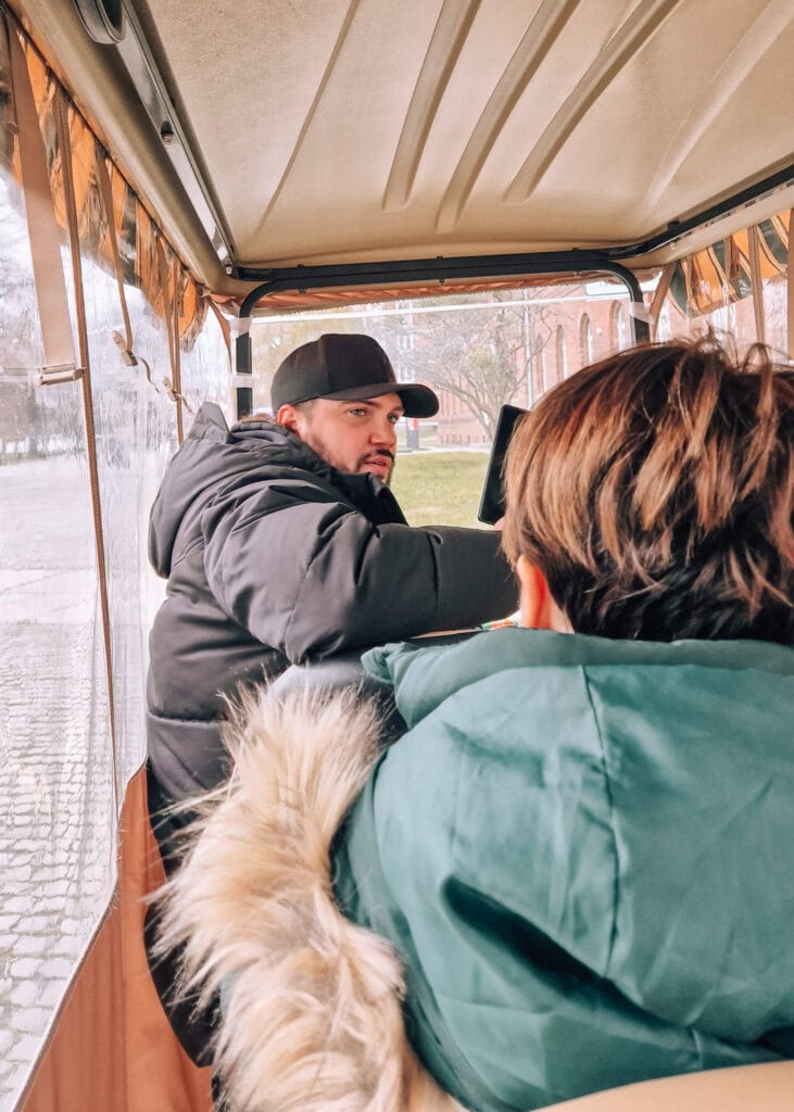 A guide sitting inside a small electric car talking to the tourists on board.