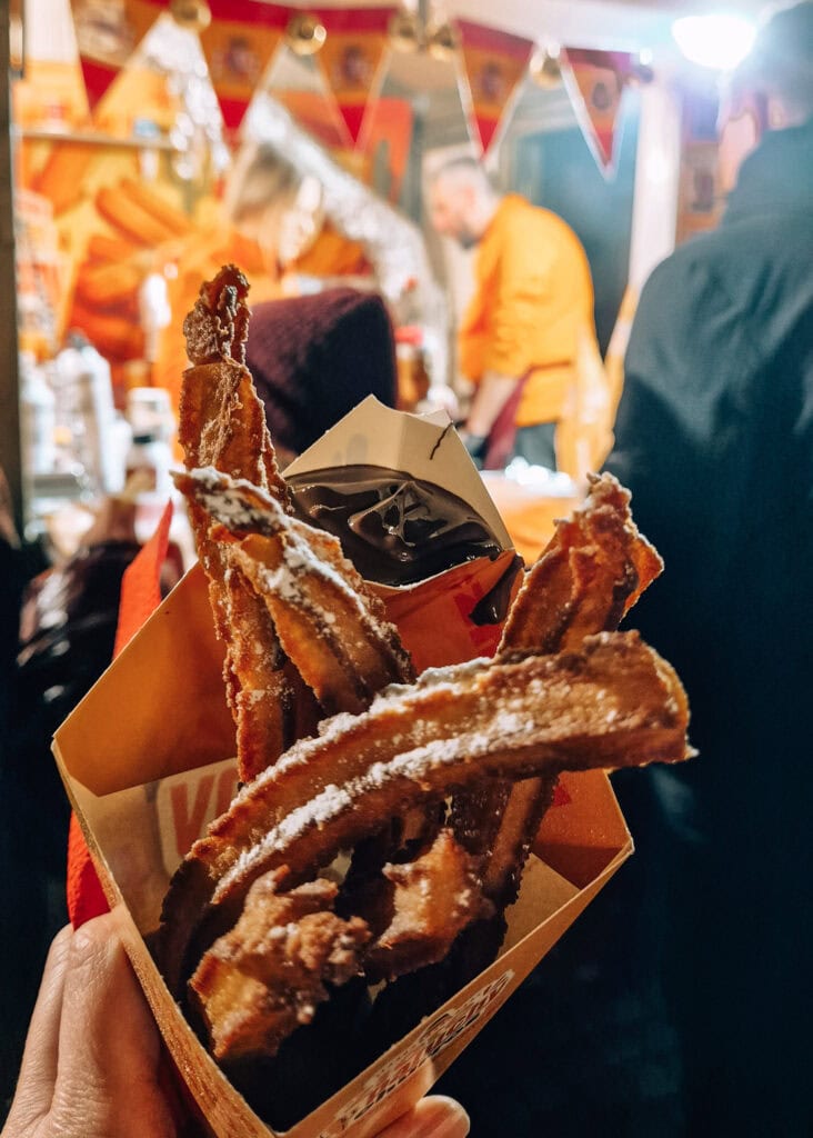 A cone with churros and chocolate saus held up in front of a food stall in Gdansk.